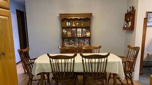 Une salle à manger avec une table et des chaises en bois, un lustre et une bibliothèque remplie de livres.