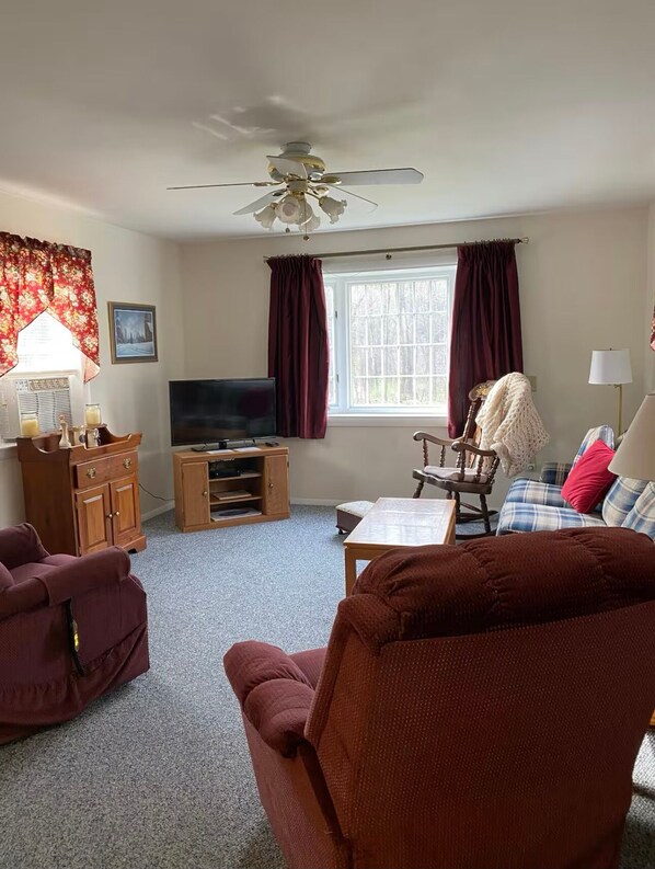 A living room with a ceiling fan, a television, a wooden cabinet, a plaid sofa, and a red armchair.