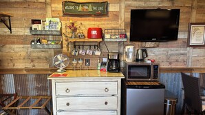A rustic kitchen with wooden walls, a mounted TV, a microwave, a coffee maker, and a small refrigerator.
