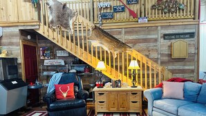A rustic cabin interior with a wooden staircase, leather furniture, and a cozy fireplace.