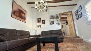 A living room with a brown leather sofa, a black coffee table, and a chandelier. There are framed pictures on the walls and a door leading to another room. - CASA RURAL LAS MARIPOSAS A HOUSE FULL OF HISTORY TO RELAX IN NAVARRE (Lerín)
