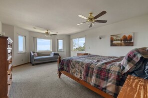 A bedroom with a bed, a bench, a dresser, two ceiling fans, and a window with a view.