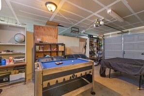 A room with a pool table, shelves with various items, and a covered bed.