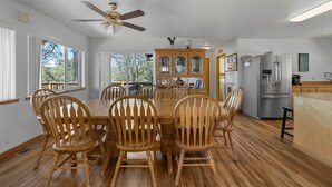 Comedor con mesa y sillas de madera, ventilador de techo y zona de cocina con refrigerador y alacenas.