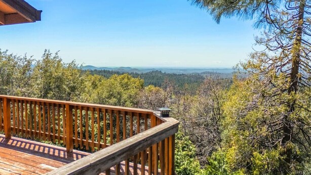 Una terraza de madera con vistas a un bosque y montañas lejanas.