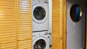 A laundry room with two stacked front-loading washing machines, wooden paneling on the walls, and a door with a round mirror. - Ramblei near Chinatown & CenterCity: 1 Bedroom - Unit A (Philadelphia)