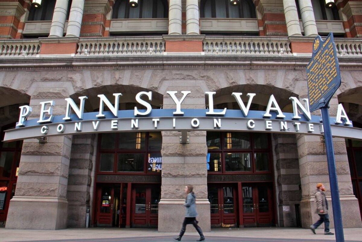 De ingang van het Pennsylvania Convention Center met een groot gebogen bord en een blauw informatiemeldbord.