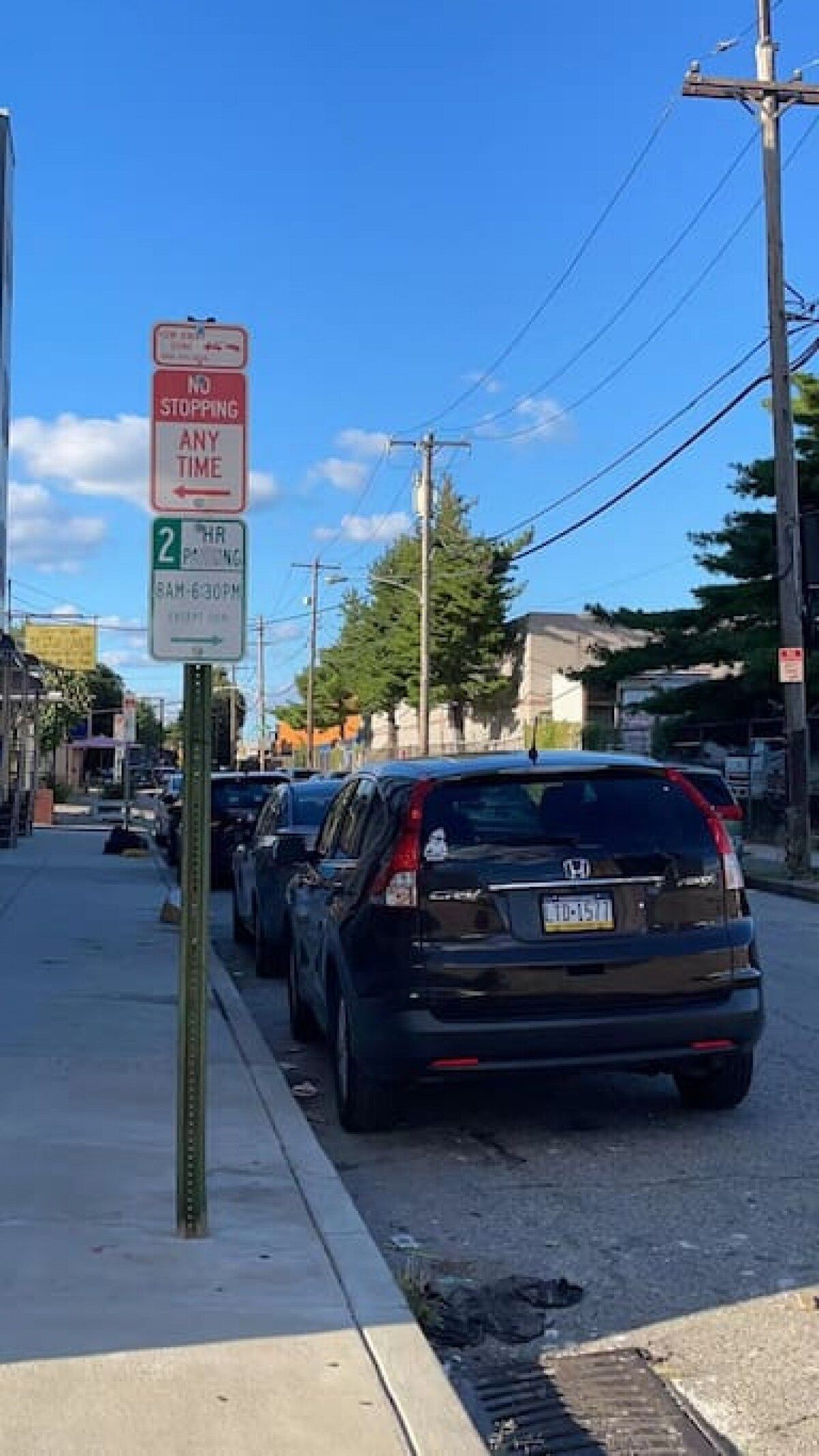 A street scene with parked cars and a sign indicating a no stopping zone.