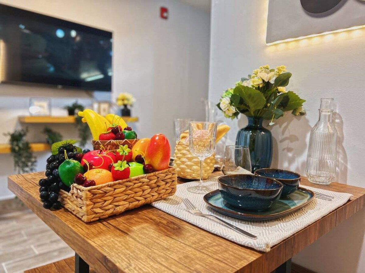 A wooden table with a fruit basket, blue bowls, and a vase with flowers.