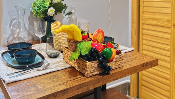 A wooden table with a fruit basket, a vase with flowers, and a wall-mounted decorative piece. - Ramblei near Chinatown & CenterCity: 1 Bedroom - Unit A (Philadelphia)