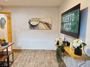 Un espace d’accueil avec un bureau en bois, un téléviseur fixé au mur qui affiche le mot « PUERTO RICO », et une œuvre d’art encadrée.