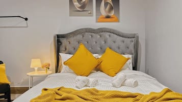 Een bed met een gestoffeerd hoofdbord, twee kussens, een opgerolde witte handdoek en een gele deken.