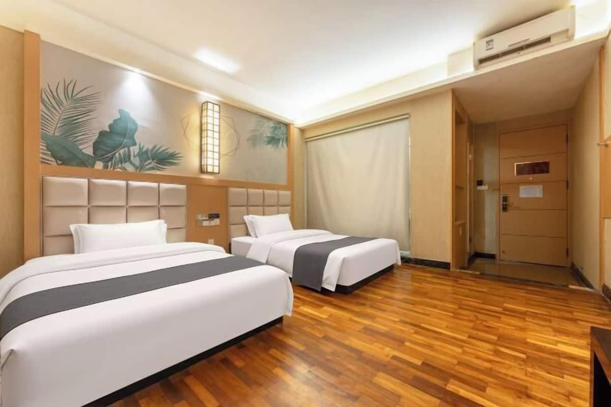 Une chambre d’hôtel avec deux lits, un plancher en bois, une grande fenêtre avec des rideaux et un mur orné d’une fresque représentant des feuilles tropicales.