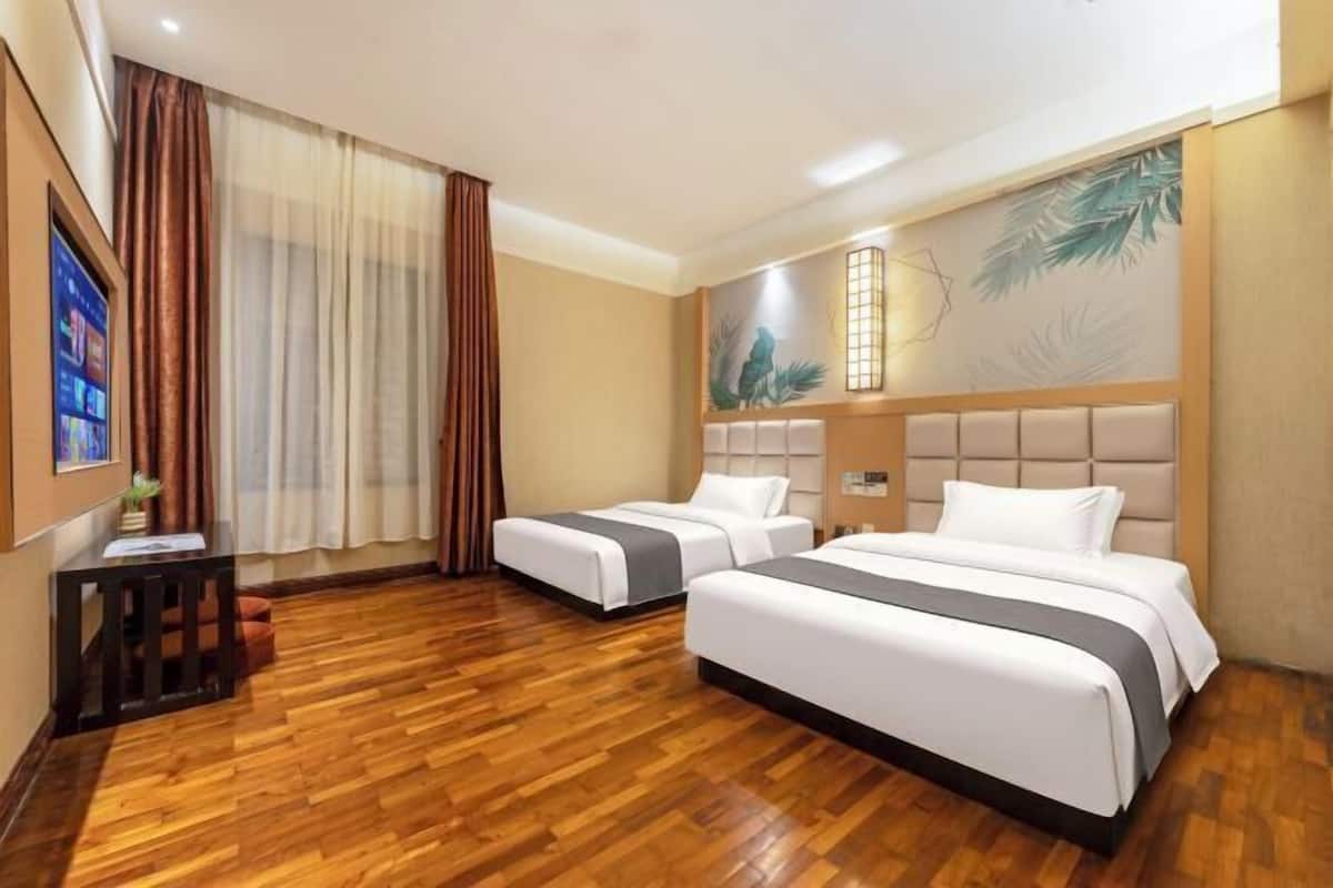 Une chambre d’hôtel avec deux lits, un plancher en bois, une grande fenêtre avec des rideaux, un téléviseur fixé au mur et un panneau décoratif mural.