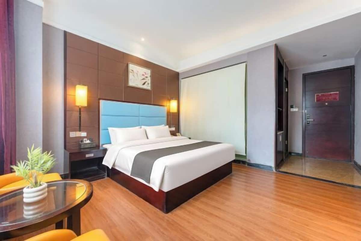Une chambre d’hôtel comprenant un lit, des tables de chevet, un bureau avec des chaises, une plante en pot et une porte coulissante.