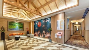 Un vestíbulo de hotel con piso a cuadros, un sofá con cojines naranjas, un cuadro de un camino y un mural con flores de cerezo.