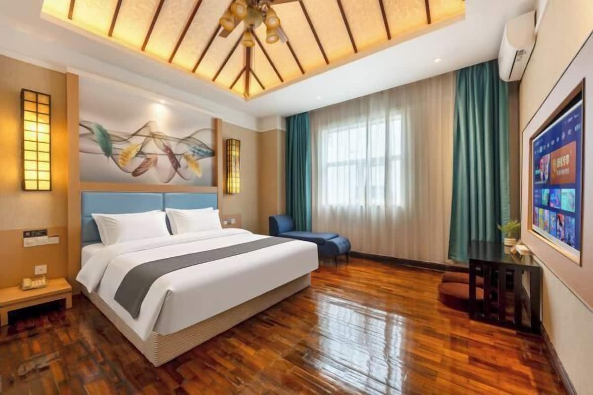Une chambre d’hôtel avec un grand lit, un bureau, une chaise, un luminaire au plafond et un téléviseur fixé au mur.