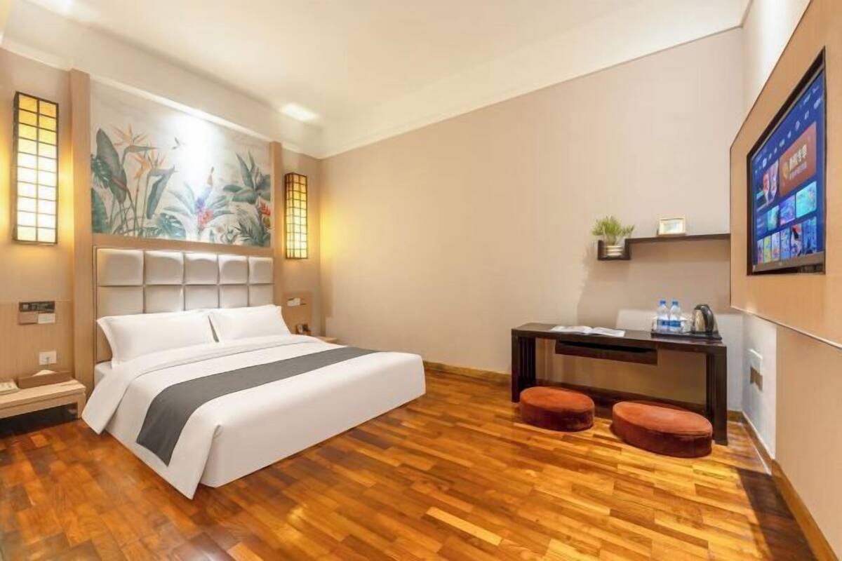 Une chambre d’hôtel avec un lit, un plancher en bois, un bureau et un téléviseur fixé au mur.