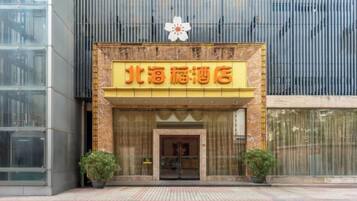 A hotel entrance with a prominent sign, a flower decoration above the sign, and two potted plants on either side of the entrance.