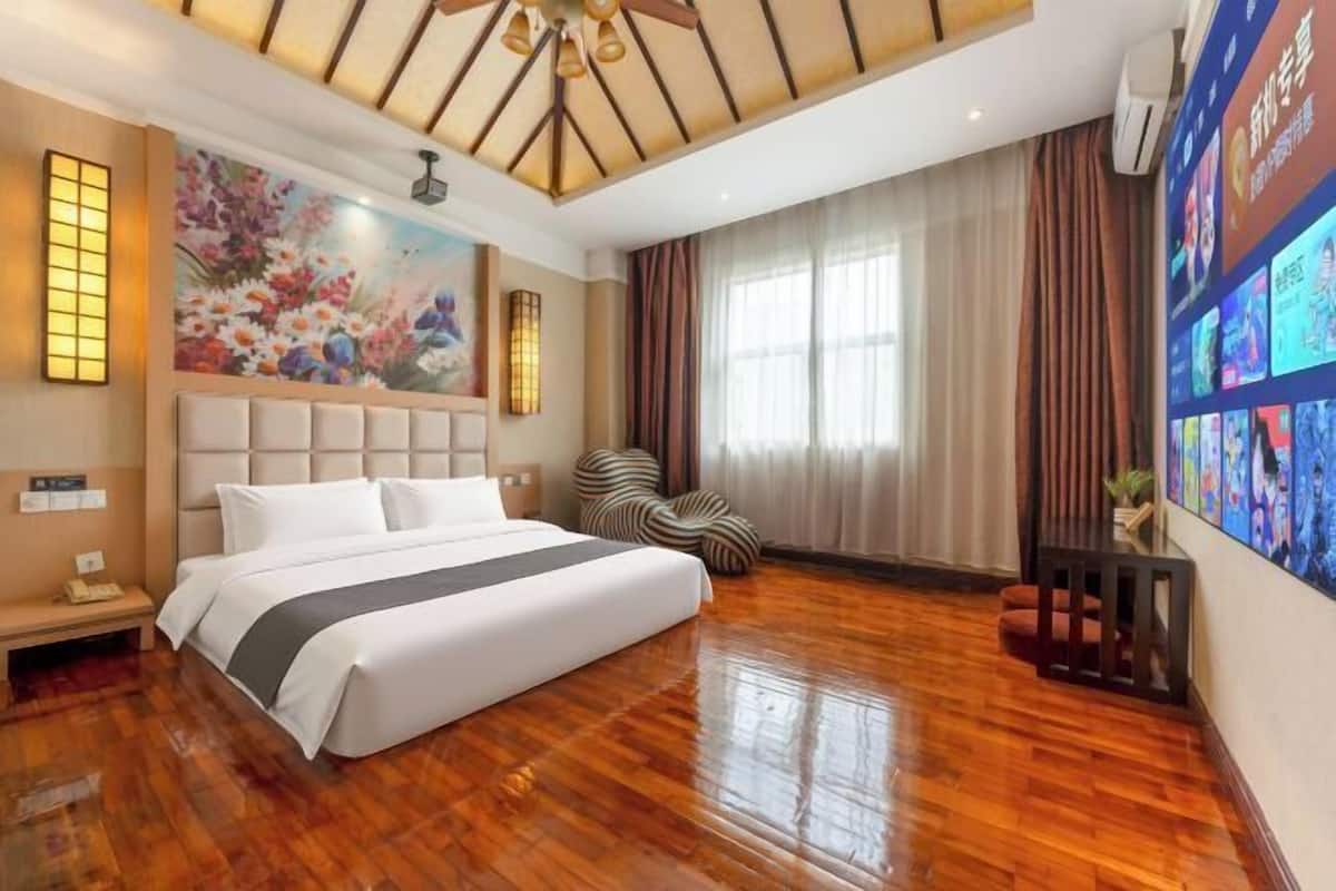 Une chambre d’hôtel avec un grand lit, un ventilateur de plafond, un tableau et un mur doté d’un écran numérique.
