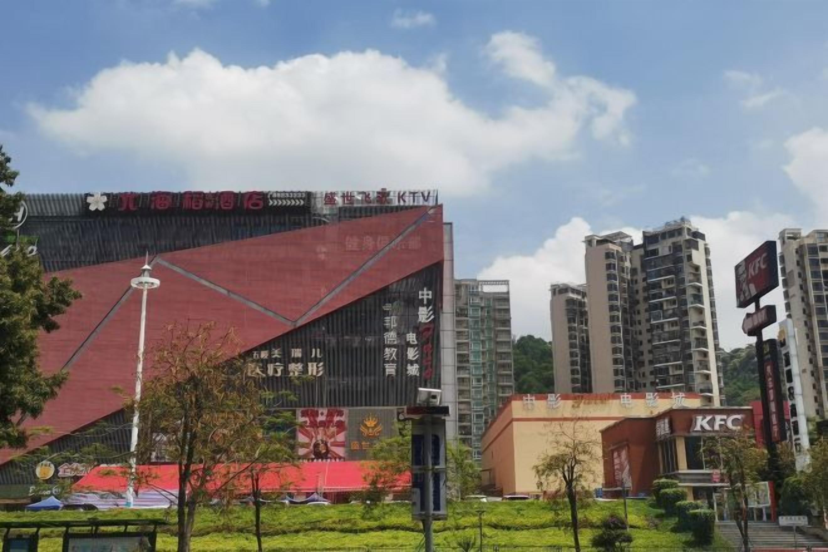 Ein modernes Gebäude mit roter Fassade, umgeben von Grünflächen und städtischer Bebauung.