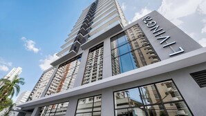 A modern high-rise building with a prominent 'LIVING' sign, featuring a sleek design with large windows and a reflective glass facade.