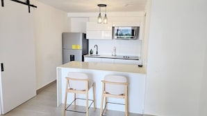 Una cucina moderna con isola centrale, due sgabelli da bar, un frigorifero, un forno a microonde e una lampada a sospensione.