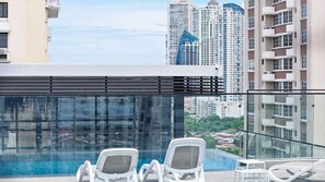Zona de piscina en la azotea con dos sillones de relax y barandilla de cristal con vistas a la ciudad.