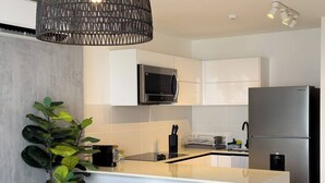 A modern kitchen with white cabinets, a stainless steel refrigerator, a built-in microwave, and a bar area with two stools. - Modern and cozy apartment in the heart of Panama City, ideal for business travelers and digital nomads. Pool, gym, and coworking space available, with valet parking offered as an optional service. (Panamá)