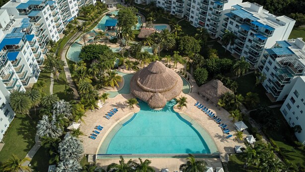Vista aérea de un resort con varias piscinas, palmeras y una piscina central grande con una estructura de techo de paja.
