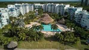 Un resort con varias edificaciones blancas, una piscina central y palmeras circundantes.