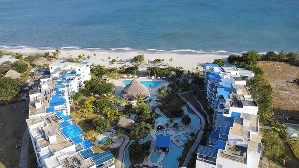 Ein Resort mit mehreren Gebäuden, einem zentralen Poolbereich und einem Strand im Hintergrund.