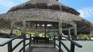 Ein Pavillon mit einem Strohdach und einer Holzterrasse, die zu einem Poolbereich führt.