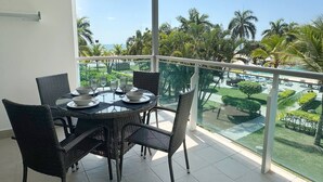 Balcón con mesa lista para comer, con vista a una piscina y palmeras.