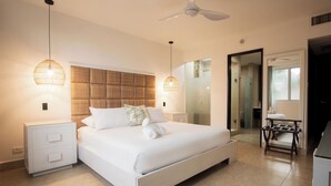 Un dormitorio moderno con una cama grande, mesitas de noche, ventilador de techo y cabina de ducha de vidrio.