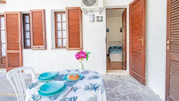 A table with blue plates and a vase of flowers, set against a white wall with wooden shutters. - Villa Bouganville   Il Gelsomino (CAPOLIVERI)