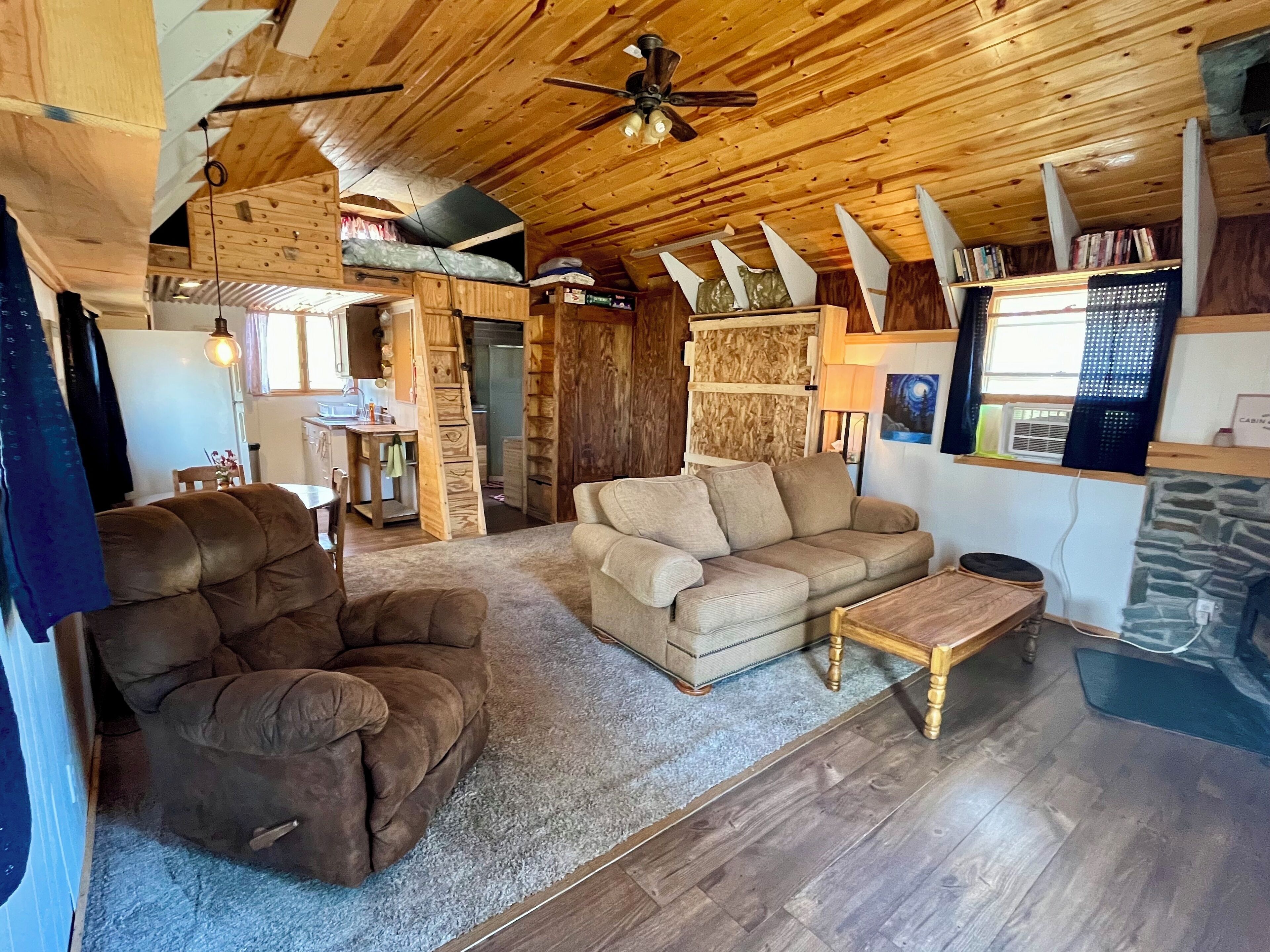 L’intérieur d’un chalet accueillant, avec un plafond en bois, un canapé, un fauteuil et une petite table.