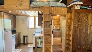 L’intérieur d’un chalet rustique, avec des murs en bois, un coin cuisine et un lit en mezzanine.