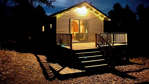 Une petite cabane dotée d’une terrasse, d’une porte-fenêtre coulissante et d’un porche avec une balustrade.