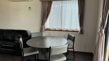 Een kamer met een ronde tafel, vier stoelen, een zwarte leren bank en een raam met gordijnen.