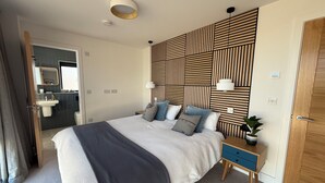 Una camera da letto moderna con un letto grande, comodini, una testiera in legno e una piccola pianta.