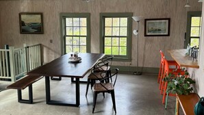 A dining area with a wooden table, chairs, and benches. There are windows with views of greenery. - More Boathouse than Lakehouse (Newcastle)