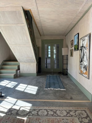 A hallway with a staircase, a door with glass panels, a lamp, and artwork on the wall.