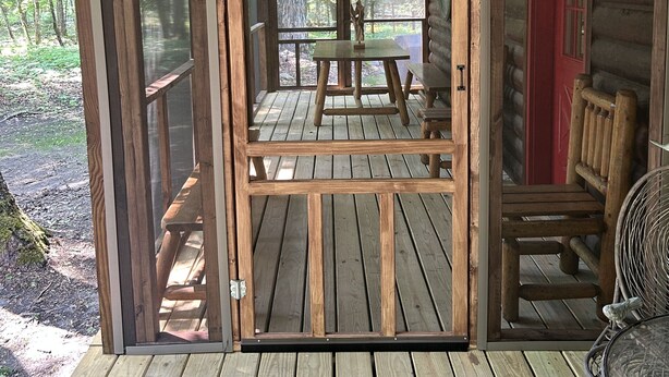 Une terrasse en bois avec une table et des chaises, une porte rouge et un lampadaire.