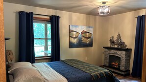 Une chambre à coucher avec un lit, une cheminée, un tableau et une vue sur l’extérieur.