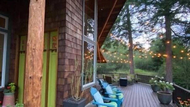 A wooden deck with blue chairs and potted plants, surrounded by trees and string lights. - Rose Mountain Lodge - Friday Harbor (Friday Harbor)