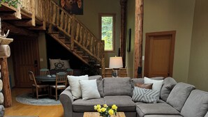 A cozy living room with a wooden staircase, a grey sectional sofa, a wooden coffee table, and a colorful rug. - Rose Mountain Lodge - Friday Harbor (Friday Harbor)