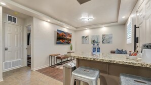 Een moderne keuken met een granieten aanrecht, roestvrijstalen barstoelen, een groot eiland en een schilderij van een zonsondergang.
