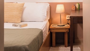 Un dormitorio con una cama, una mesita de noche con lámpara, un taburete de madera y una ventana que ofrece vistas a árboles.