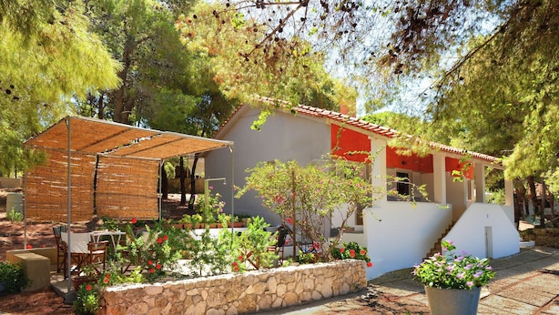 Un patio con una mesa y sillas, una jardinera de piedra con flores y un pequeño edificio con techo rojo.